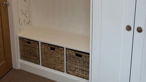 A white wardrobe with a floral wallpaper design, a wooden door, and three wicker baskets at the bottom.