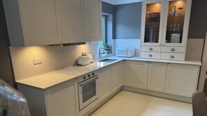 A modern kitchen with white cabinetry, a built-in oven, a sink, and a countertop with a toaster and a kettle. - Cairn - one bedroom apartment sleeps up to three (Midlothian)
