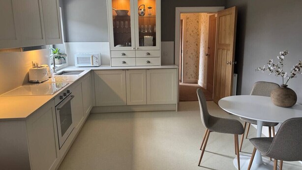A modern kitchen with white cabinets, a built-in microwave, and a dining area with a round table and chairs. - Cairn - one bedroom apartment sleeps up to three (Midlothian)