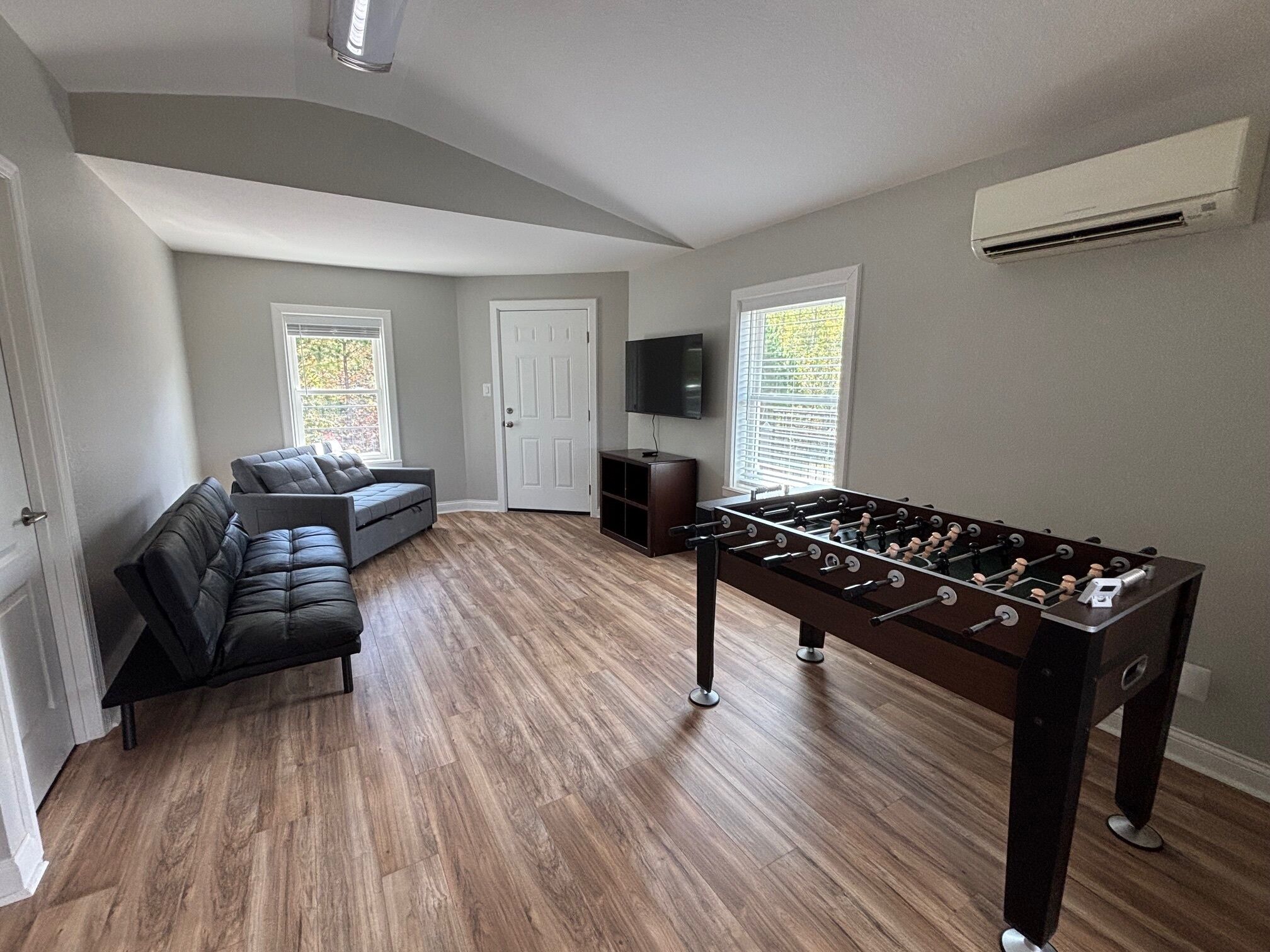 A living room with a dark-colored sofa, a foosball table, and a television on a stand.