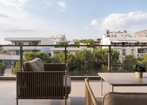 Un balcone con un divano e un tavolo, affaccia su un panorama urbano con edifici e aree verdi.