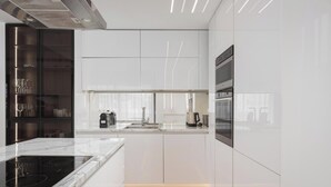 Uma cozinha moderna com armários brancos, um fogão por indução preto e eletrodomésticos de aço inoxidável.