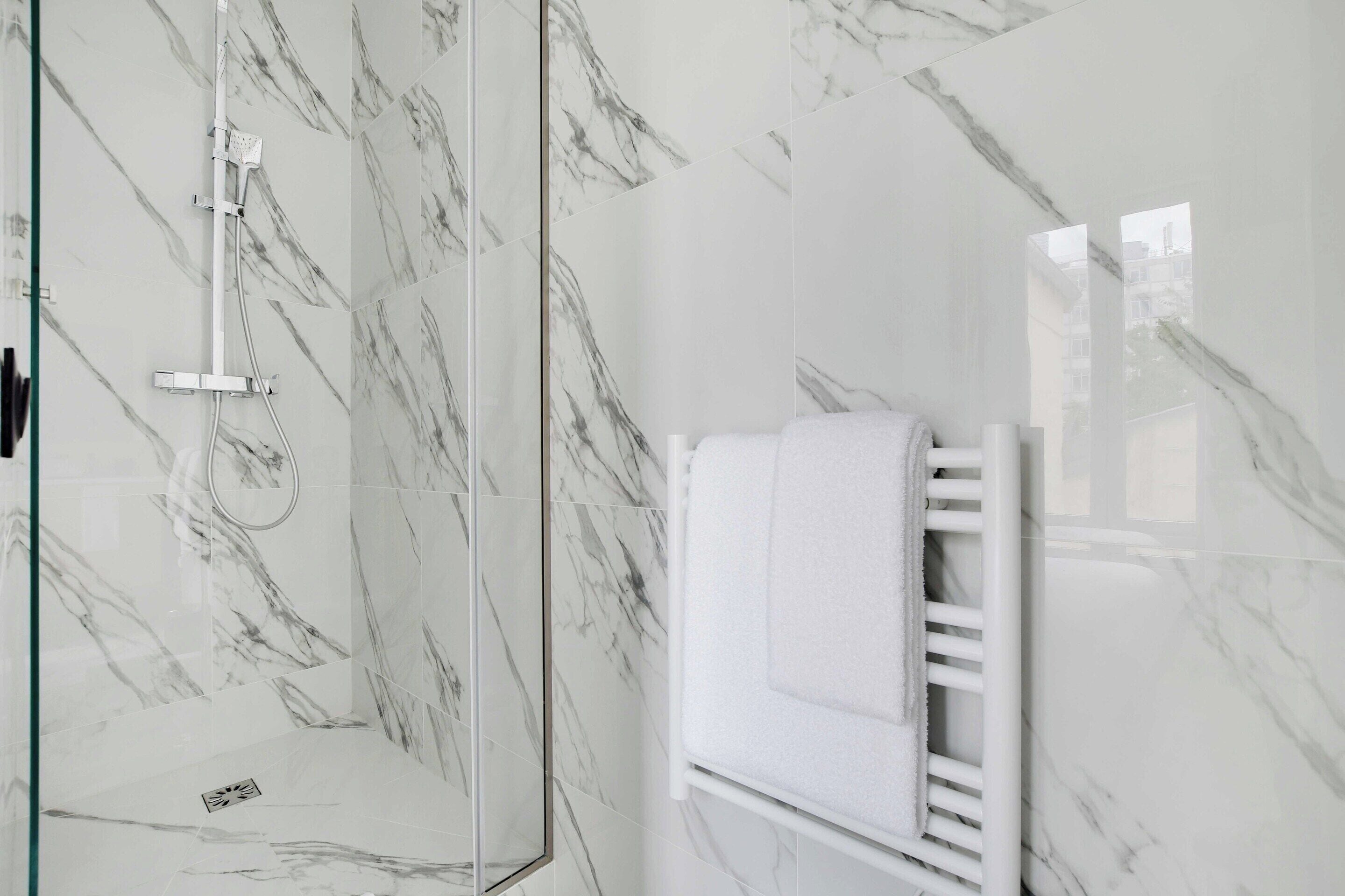 A bathroom with a glass shower enclosure, a white towel rack, and marble-patterned walls.