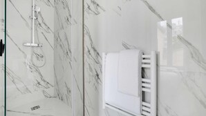 Une salle de bain dotée d’une douche à parois de verre, de carreaux de marbre blanc et d’un porte-serviettes blanc.