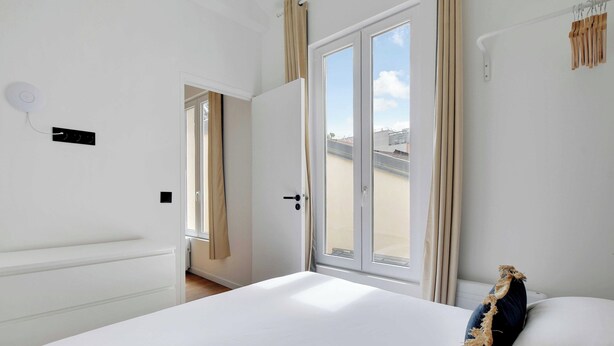 Une chambre avec un grand lit, une porte donnant sur un balcon et un luminaire fixé au mur.