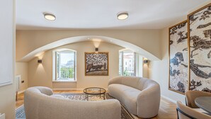 A spacious living room with high ceilings, a large window, and a view of the city. There are two bean bag chairs, a small round table, and a patterned rug.