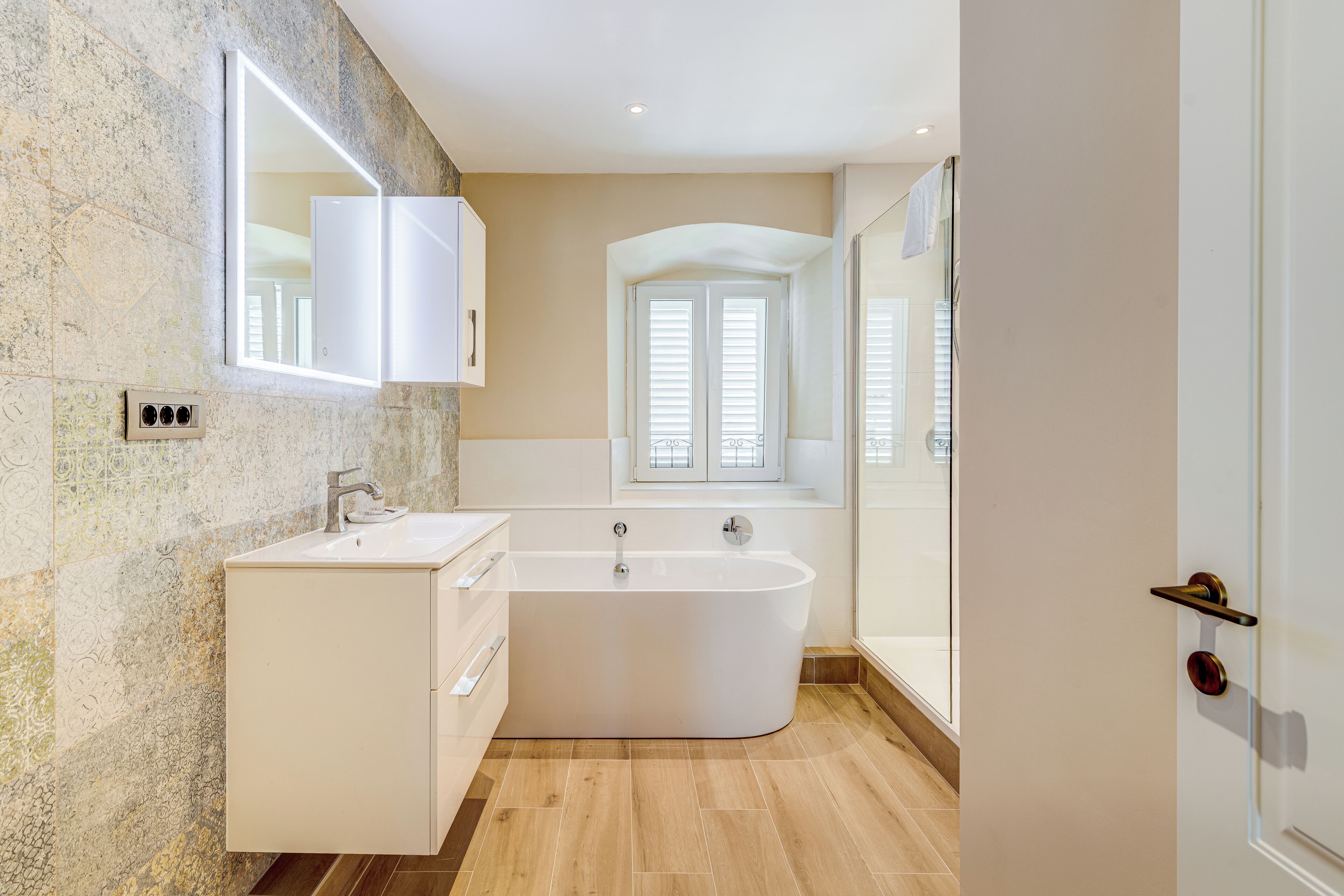 Une salle de bain moderne avec une baignoire sur pieds, un meuble-lavabo avec un miroir et une fenêtre avec des volets.
