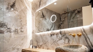 A modern bathroom with marble walls, a stone sink, and a wooden bench. - Ode Aristofanous - Urban Hotel (Athens)