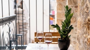 A table with two wine glasses and a potted plant on a balcony with stone walls and metal railings. - Ode Aristofanous - Urban Hotel (Athens)