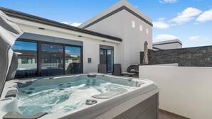 Ein moderner Whirlpoolbereich im Freien mit einer Steinmauer, einem Sonnenschirm und Blick auf das Haus.