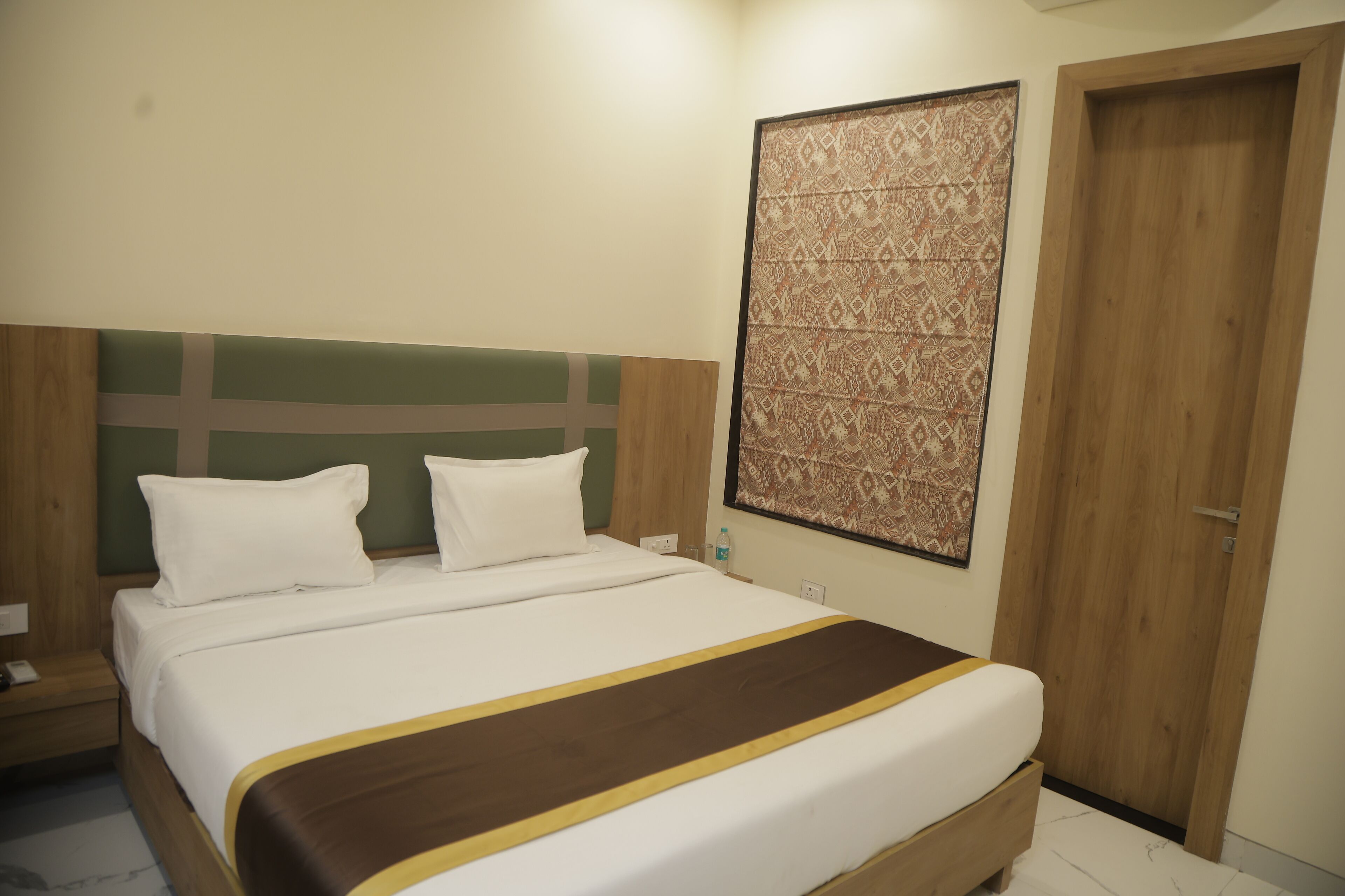 Una cama bien hecha con ropa de cama blanca y marrón, un cabecero de madera, una obra de arte colgada en la pared y una puerta de madera.
