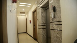 Ein Hotelgang mit Marmorwand, Aufzug und Feuerlöscher.