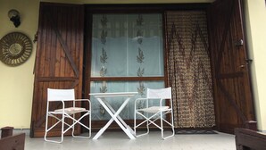 Een terras met twee witte stoelen en een kleine tafel, een houten deur en een decoratief wandbord.
