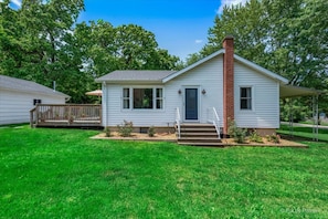 A single-story house with a front porch, a chimney, and a small garden area.
