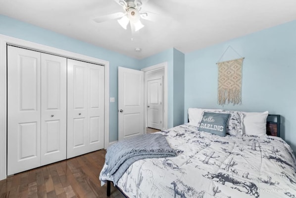 A bedroom with a bed, a ceiling fan, and a wall-mounted macrame piece.