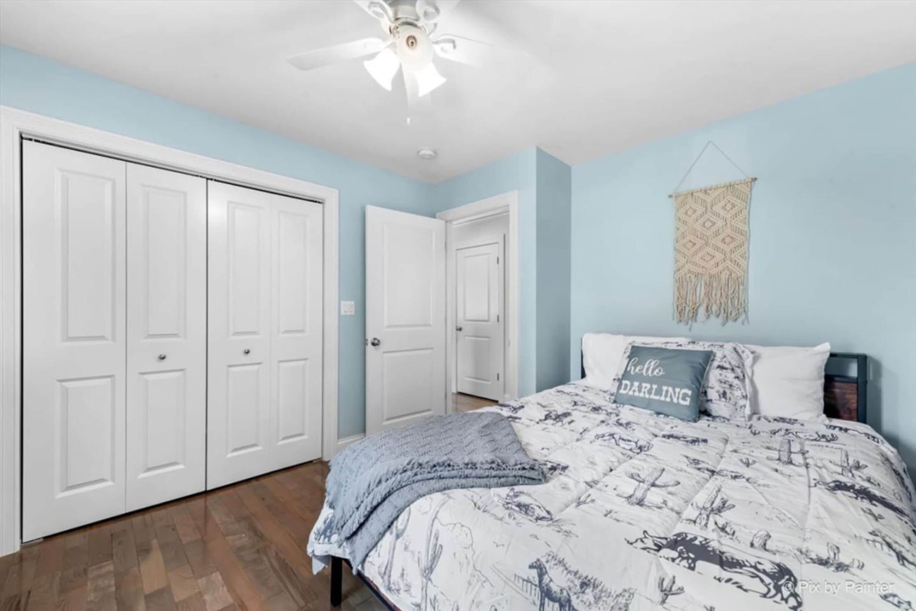 A bedroom with a bed, a ceiling fan, and a wall-mounted macrame piece.