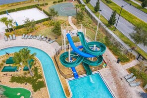 Un espace piscine équipé d’un toboggan, de chaises longues et d’un terrain de basketball.