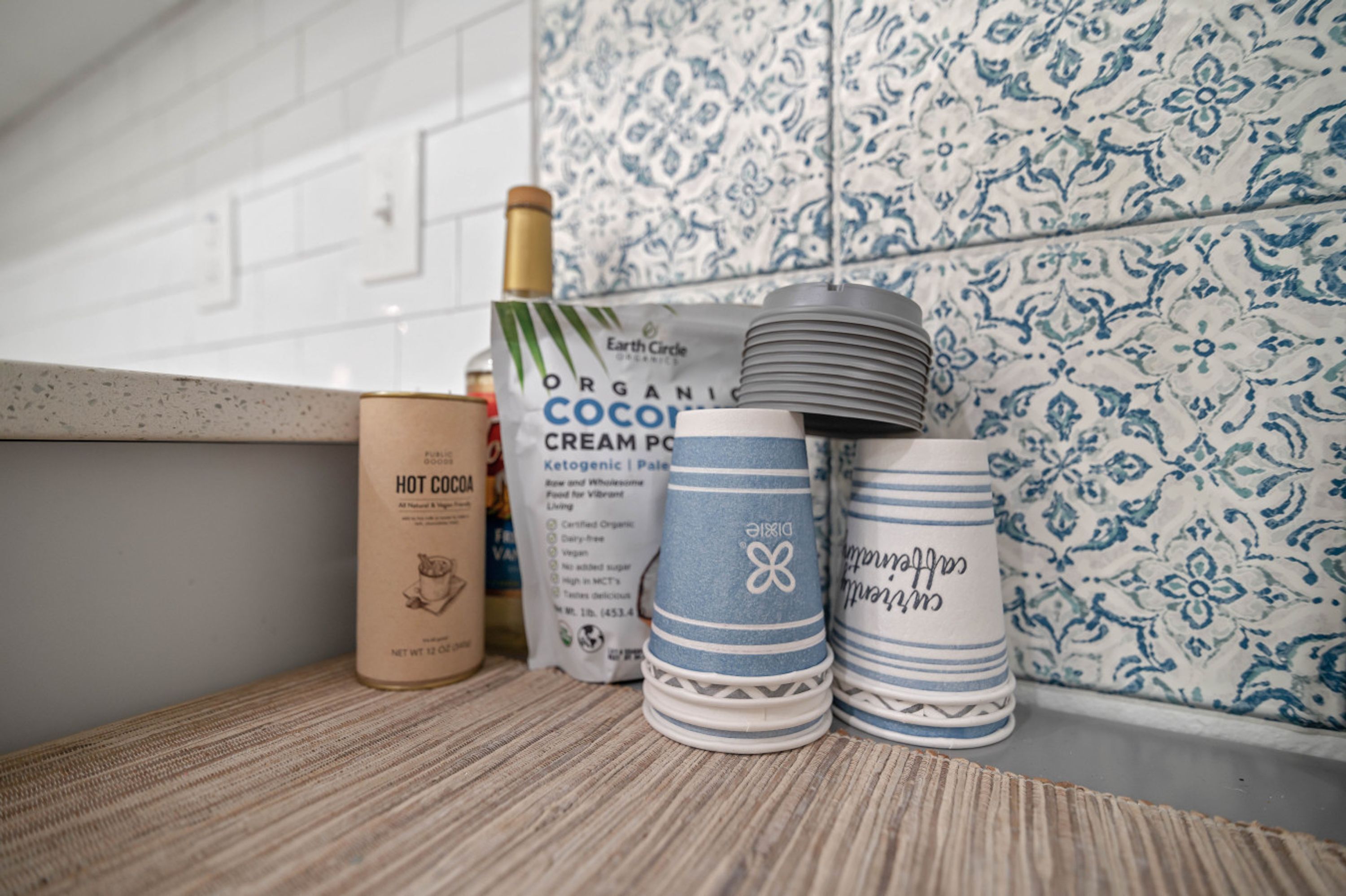 A kitchen counter with a bottle of hot cocoa, a bag of organic cream powder, and stacked plates.