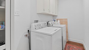 Une buanderie avec un lave-linge blanc, un étendoir et des placards au-dessus.