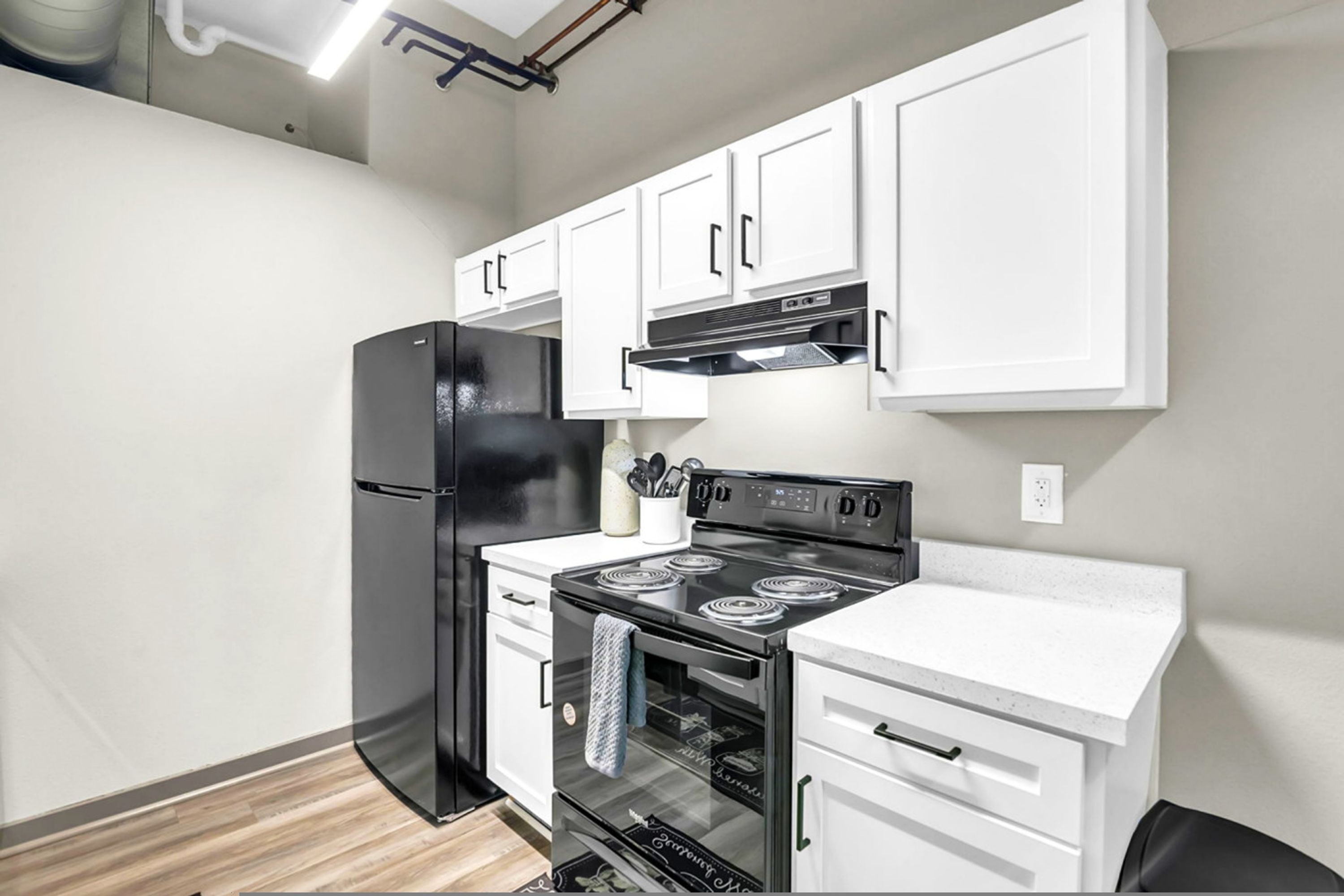 A compact kitchen with white cabinets, a black refrigerator, a stove, and a microwave.