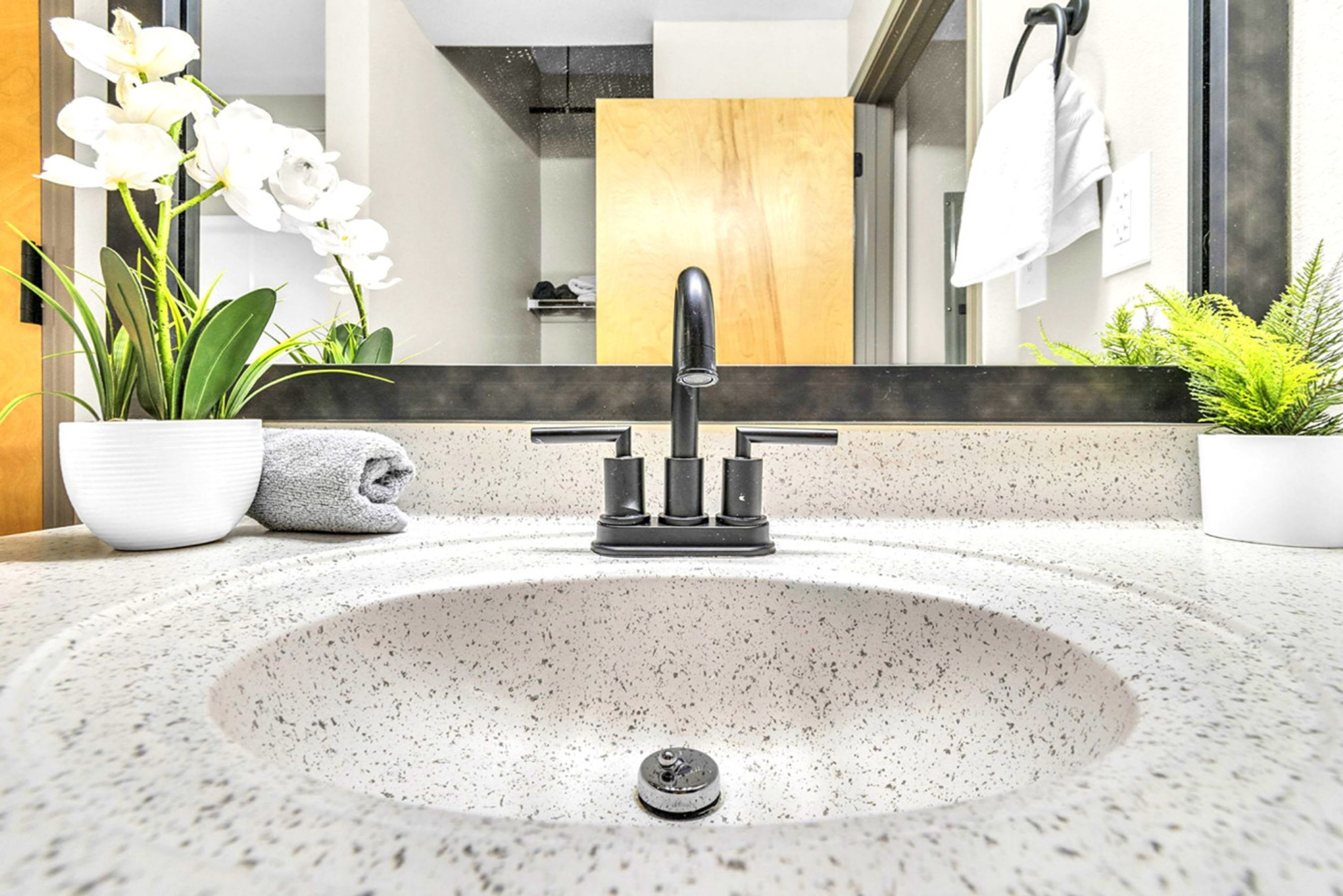A modern bathroom with a freestanding sink, a mirror, and potted plants.