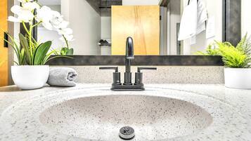 A modern bathroom with a freestanding sink, a mirror, and potted plants.