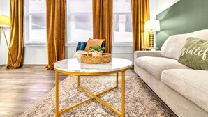 Una sala de estar con un sofá, una mesa redonda de centro, una lámpara y una ventana con cortinas.