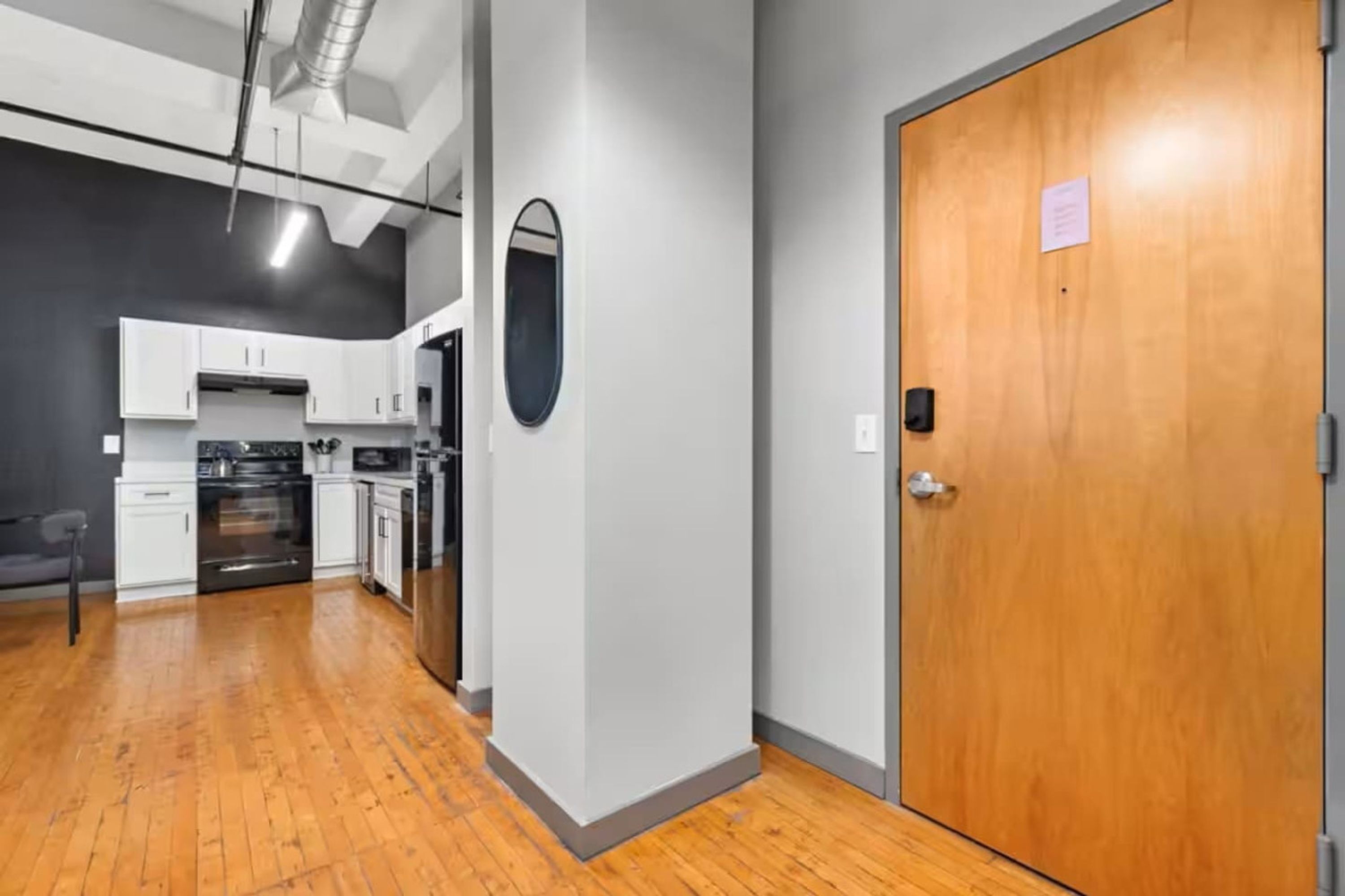 A modern kitchen with white cabinets, a built-in oven, and a wooden floor.