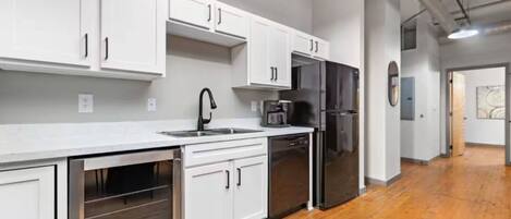 A modern kitchen with white cabinets, stainless steel appliances, and a wooden floor.