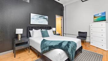 Ein modernes Schlafzimmer mit Bett, Nachttischen, Kommode, Sessel und Fernseher.