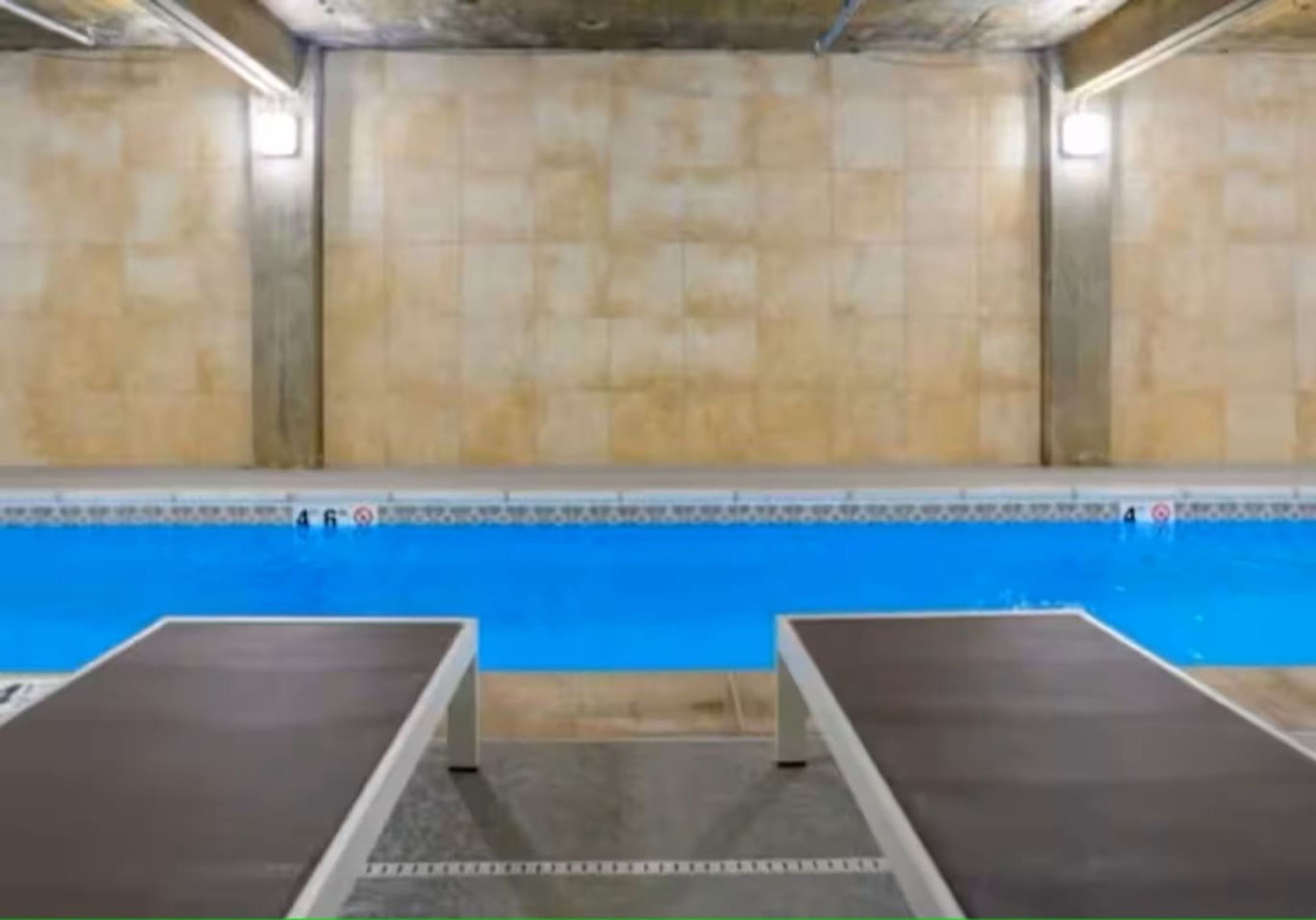 Une piscine avec deux chaises longues au premier plan et des murs carrelés en arrière-plan.