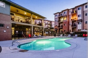 A pool area with lounge chairs, a covered patio, and multi-story residential buildings. - Modern Retreat in West Des Moines (West Des Moines)