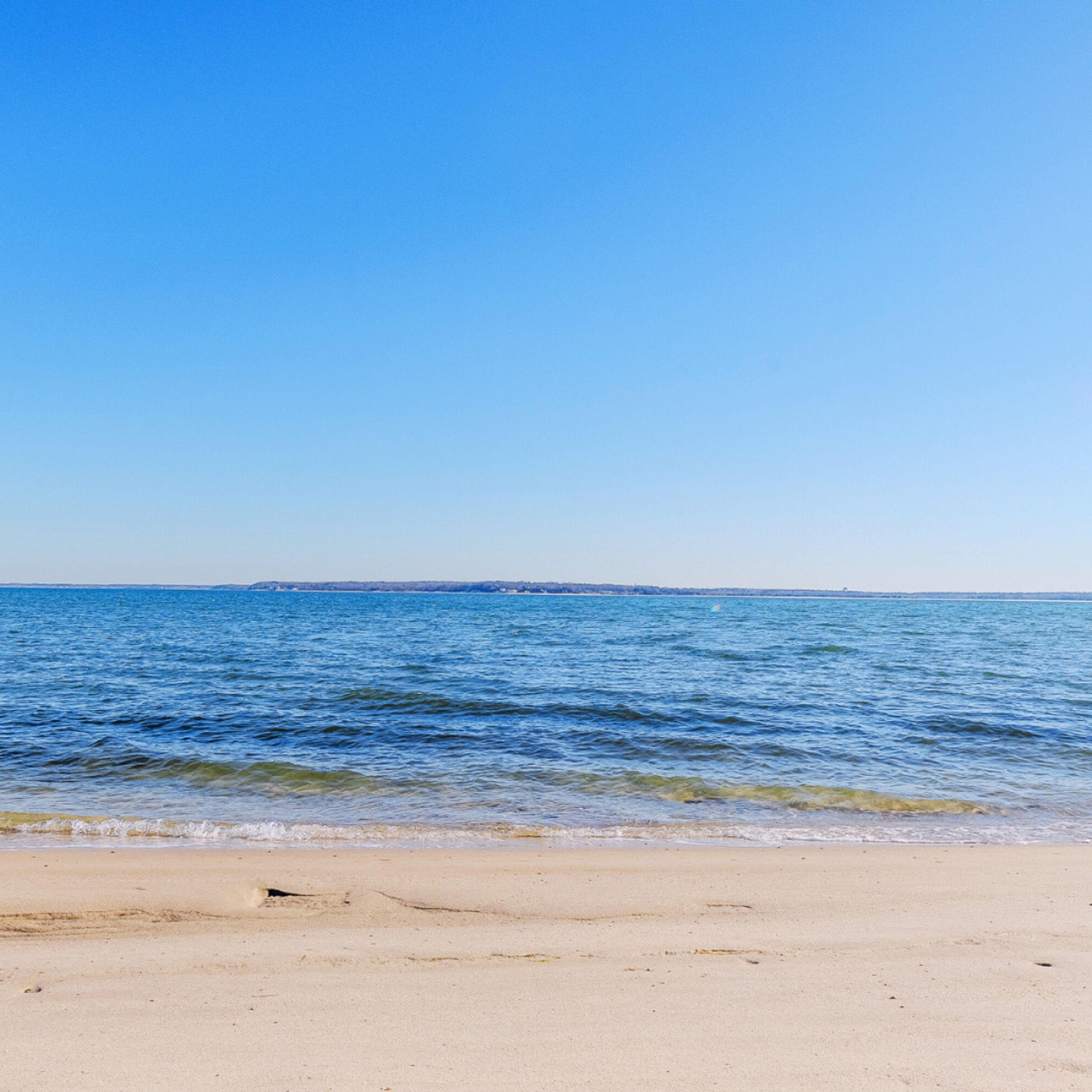 A beach with clear blue water and a sandy shore.