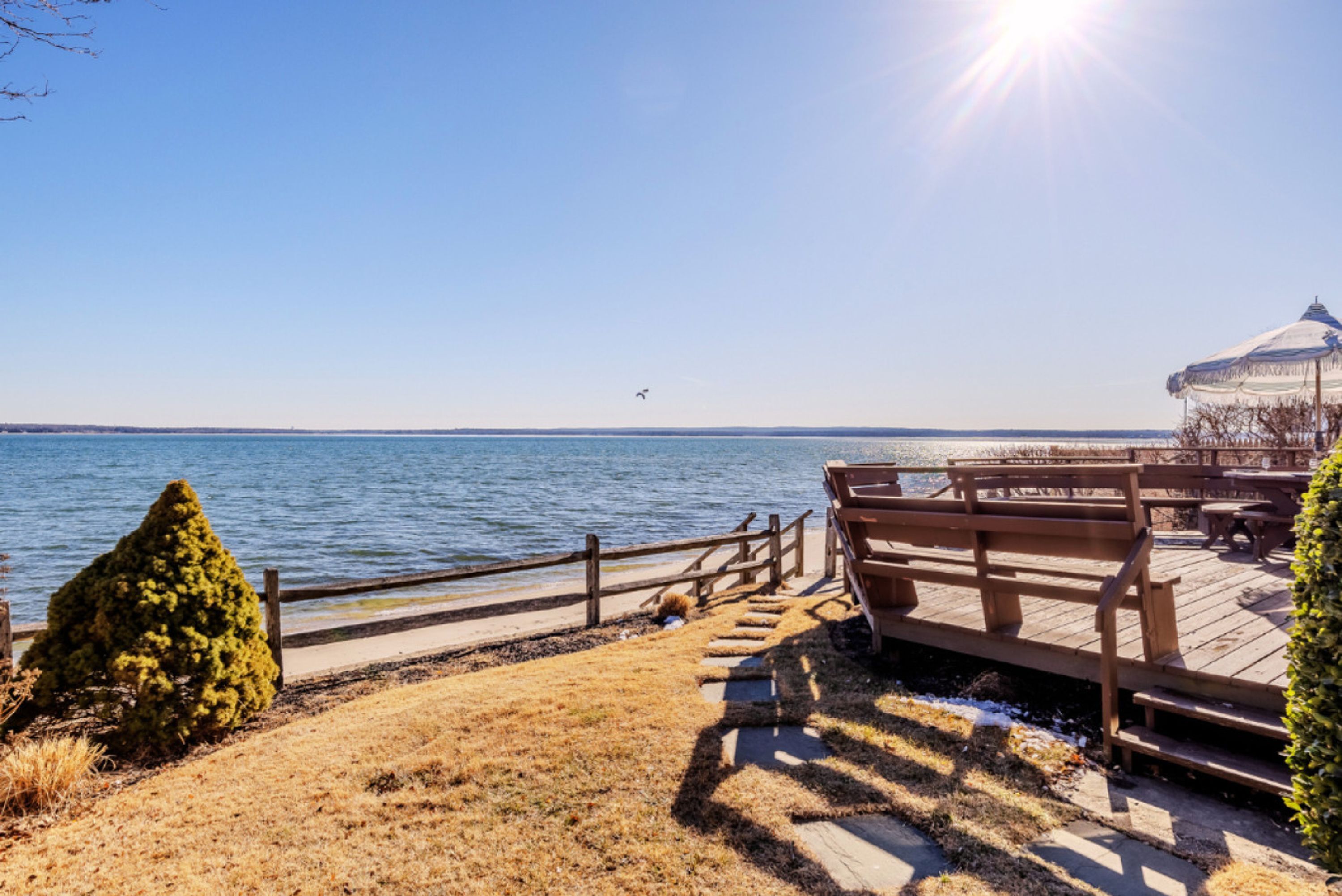A wooden deck with benches overlooking a body of water, a gazebo, and a clear sky.
