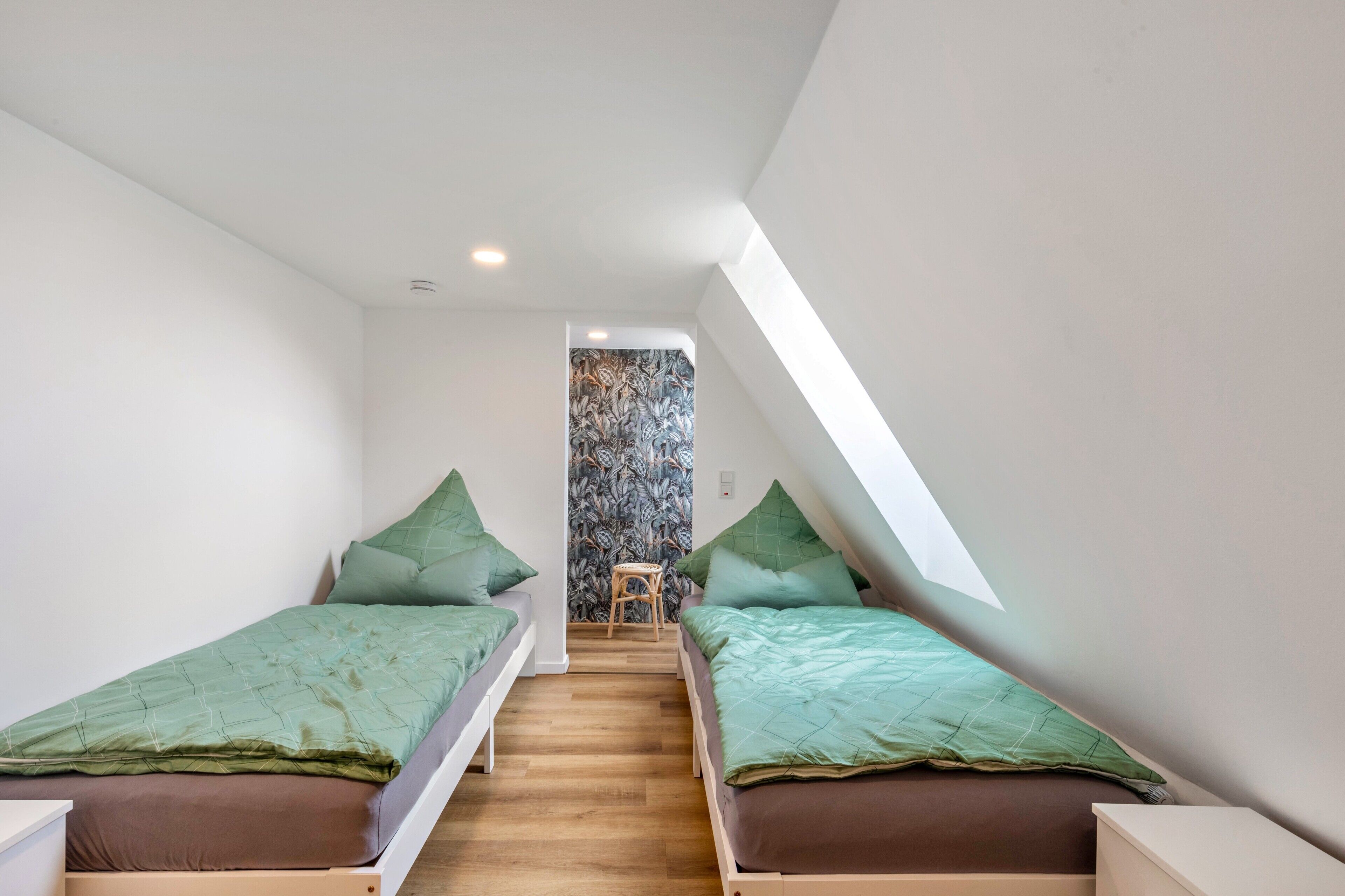 Ein kleiner, moderner Raum mit zwei Einzelbetten, Holzboden und einer Treppe zu einem Schlafbereich auf einer Zwischenebene.
