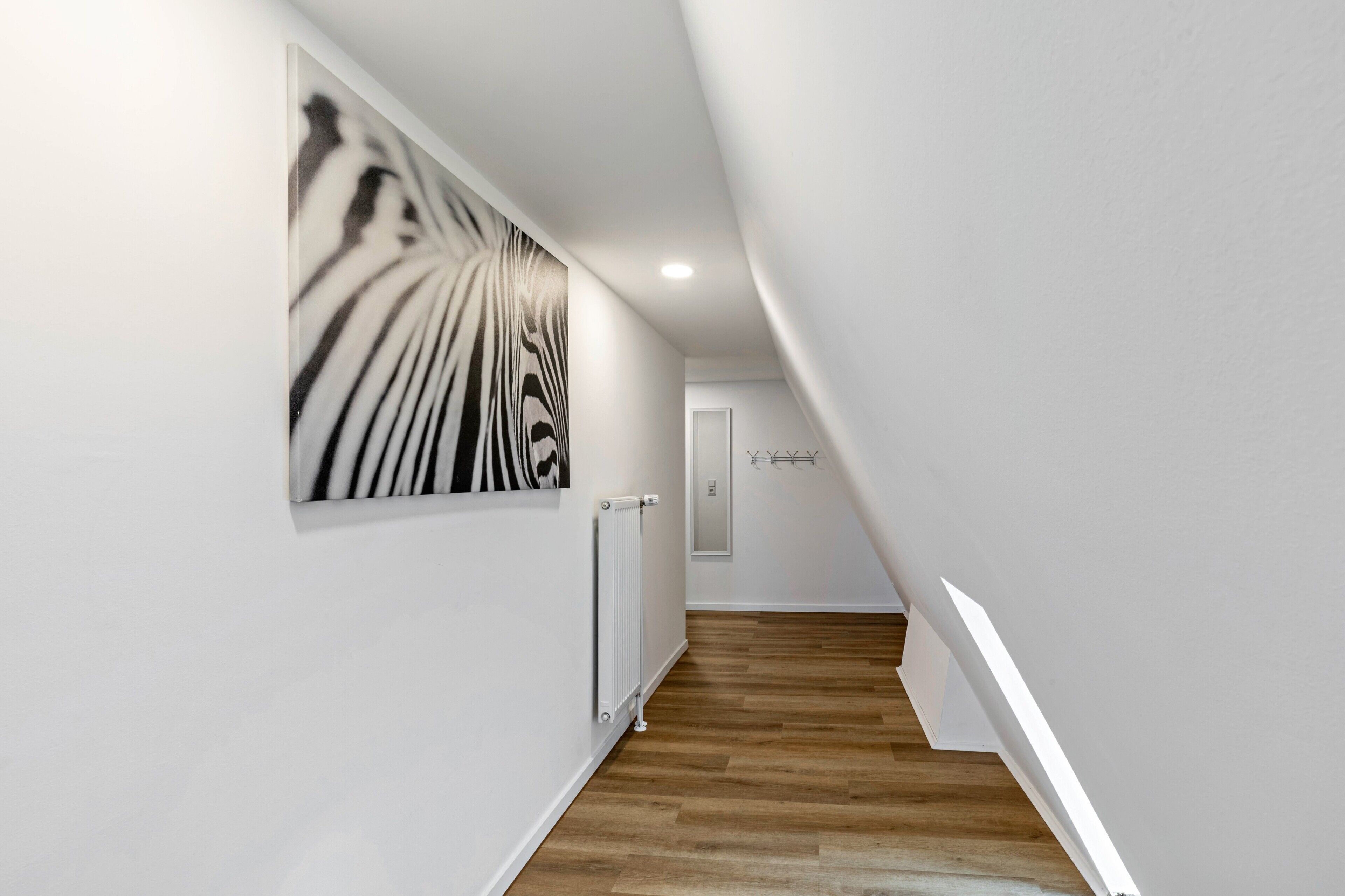 Un pasillo moderno con suelo de madera, paredes blancas y una obra de arte abstracta de gran tamaño.