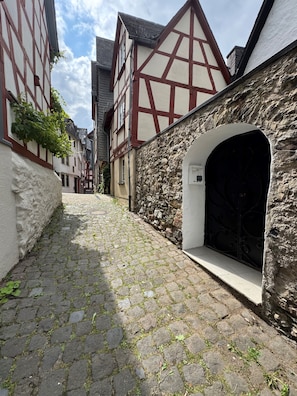 A cobblestone street flanked by traditional half-timbered buildings with a stone wall and an arched entrance.