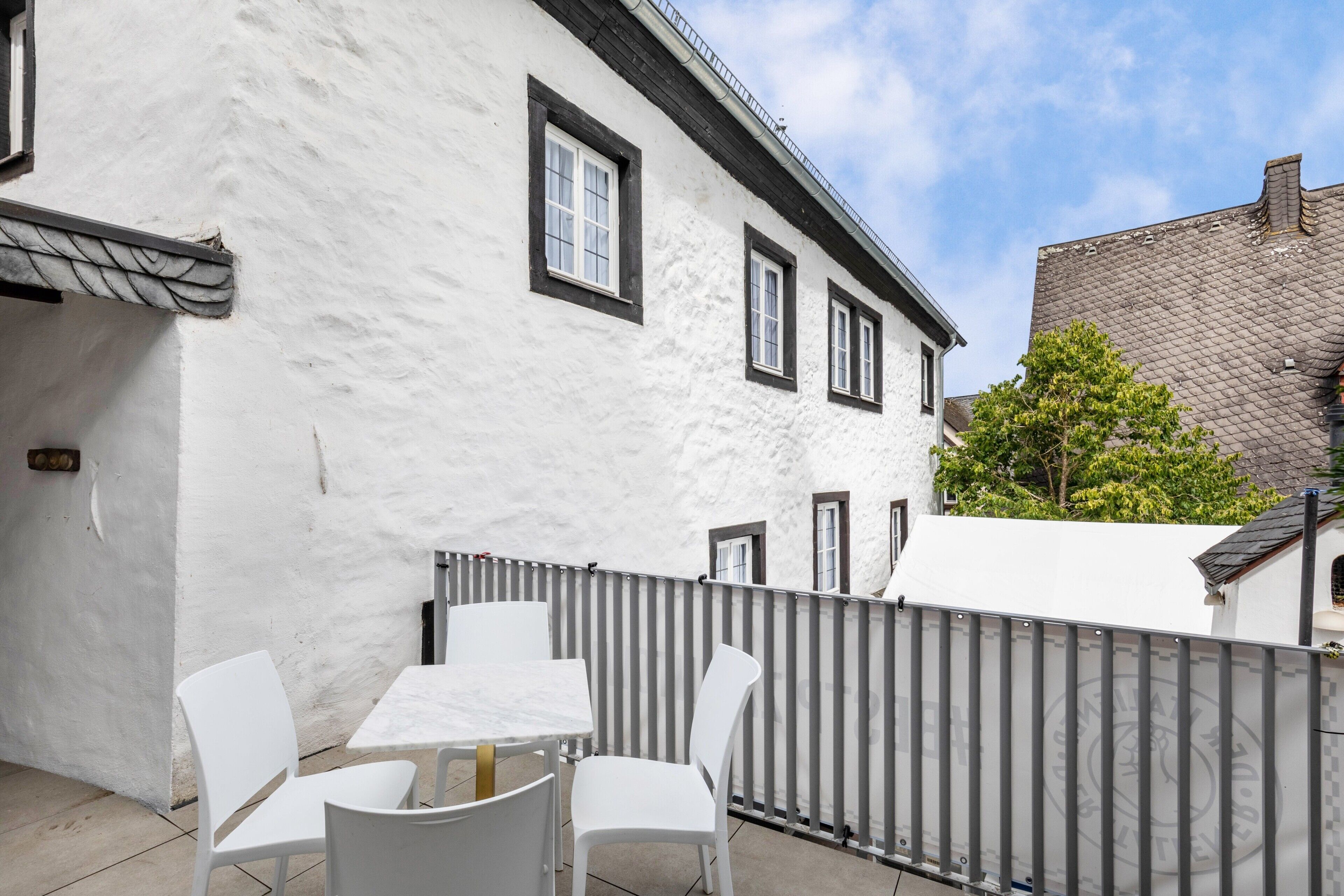 Een wit gebouw met een balkon, een tafel en vier stoelen.