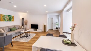 Una sala de estar moderna con un sofá, una mesa de centro, un televisor de pantalla plana y una zona de comedor con una mesa y sillas.