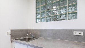 A kitchen with a stainless steel sink, white cabinets, and a window with frosted glass.
