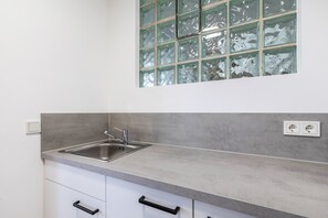 A kitchen with a stainless steel sink, white cabinets, and a window with frosted glass.