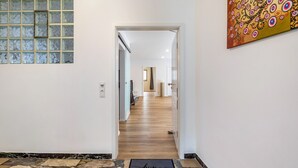 A hallway with a stone-tiled floor, a glass block wall, and a wooden door leading to a room.