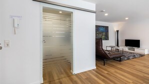 A modern living room with a sliding glass door, a flat-screen TV, a brown leather sofa, and a painting on the wall.