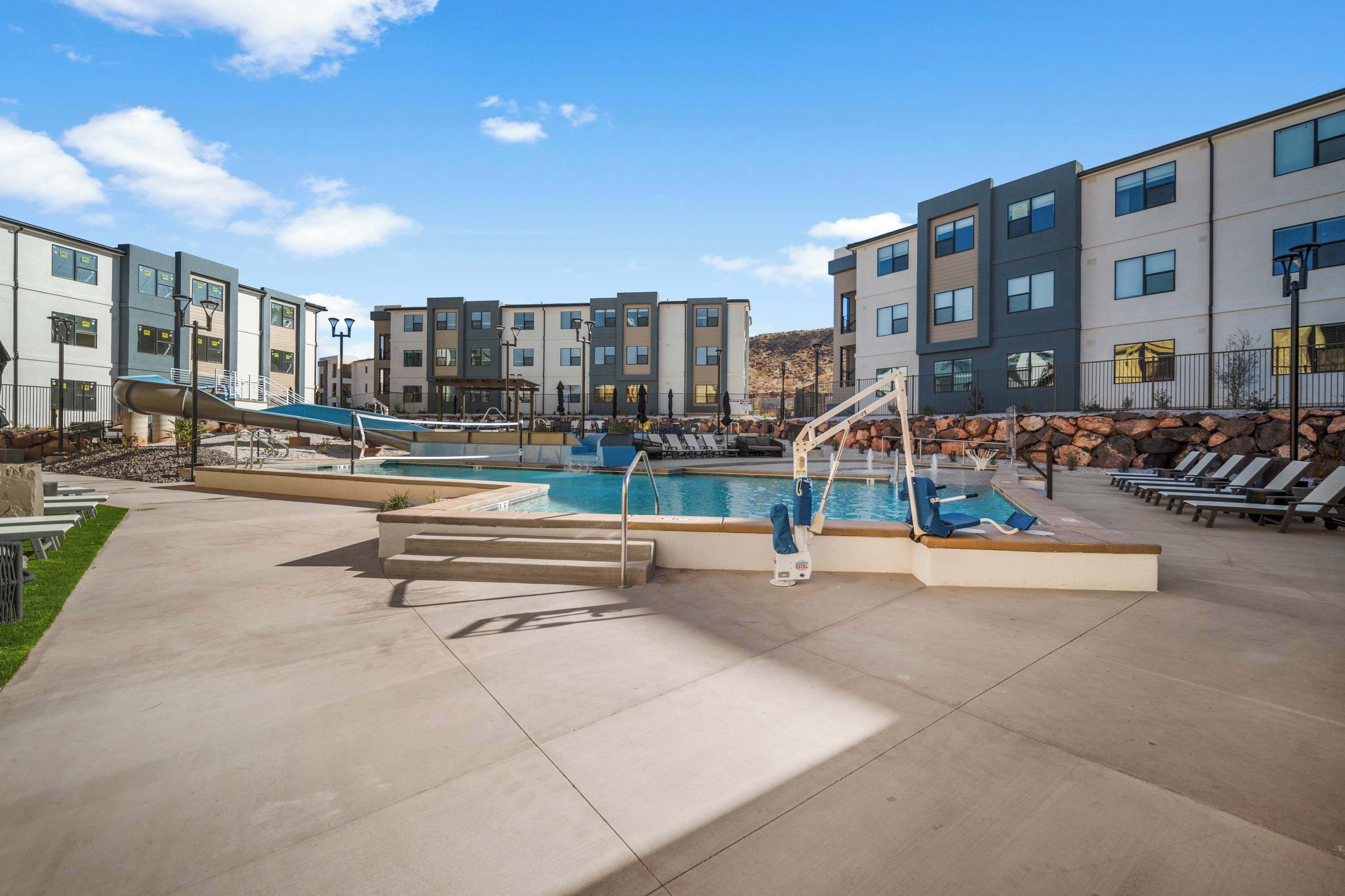 Un espace piscine extérieur moderne, doté d’un toboggan, de chaises longues et d’un mur en pierre.