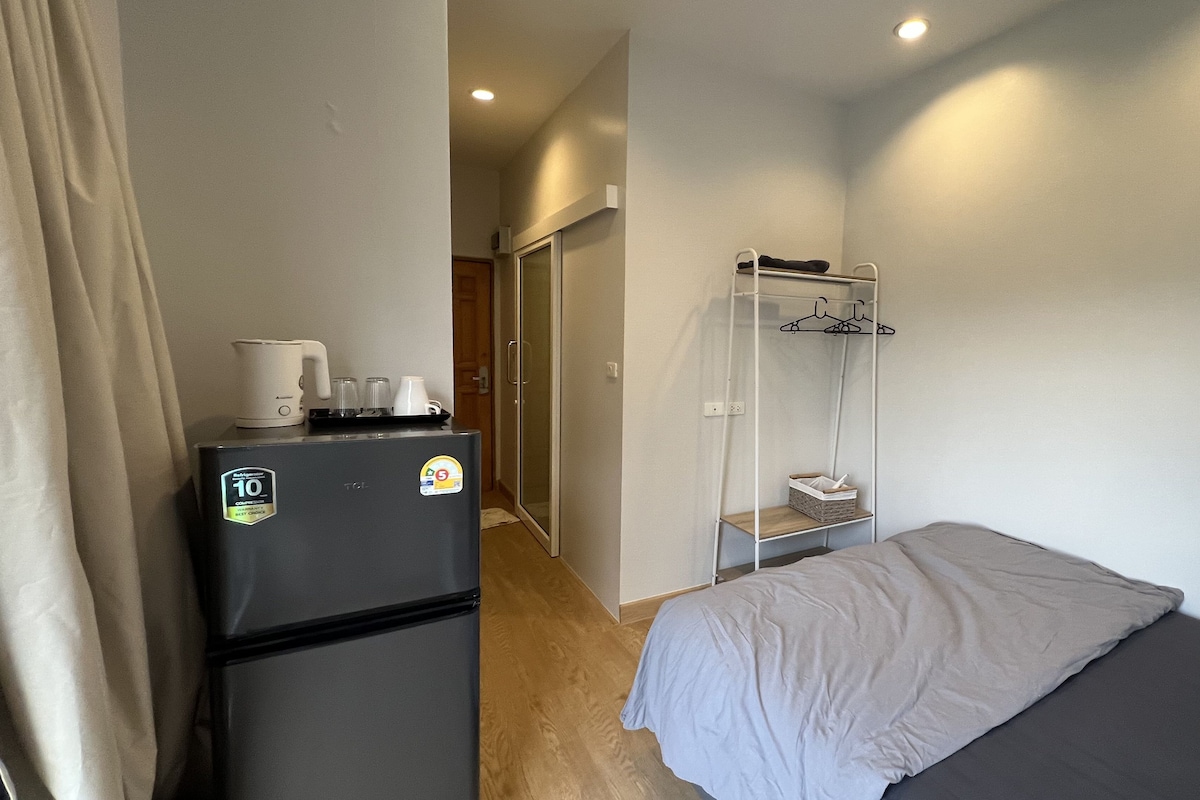 A compact room with a bed, a small kitchenette with a refrigerator, and a wardrobe with hanging space.
