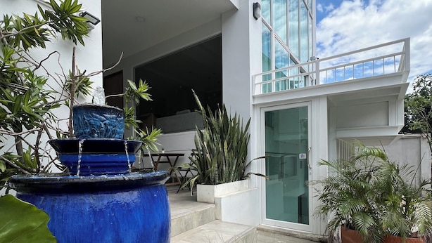 A modern building with a blue water feature in the foreground, potted plants, and a clear sky. - Calm and Green Place (Chiang Mai)