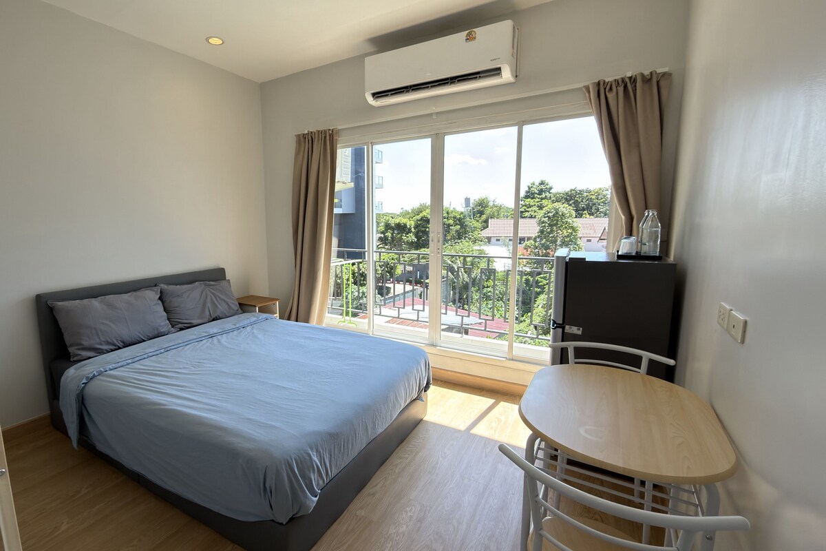 A bedroom with a bed, a desk, and a balcony with a view.