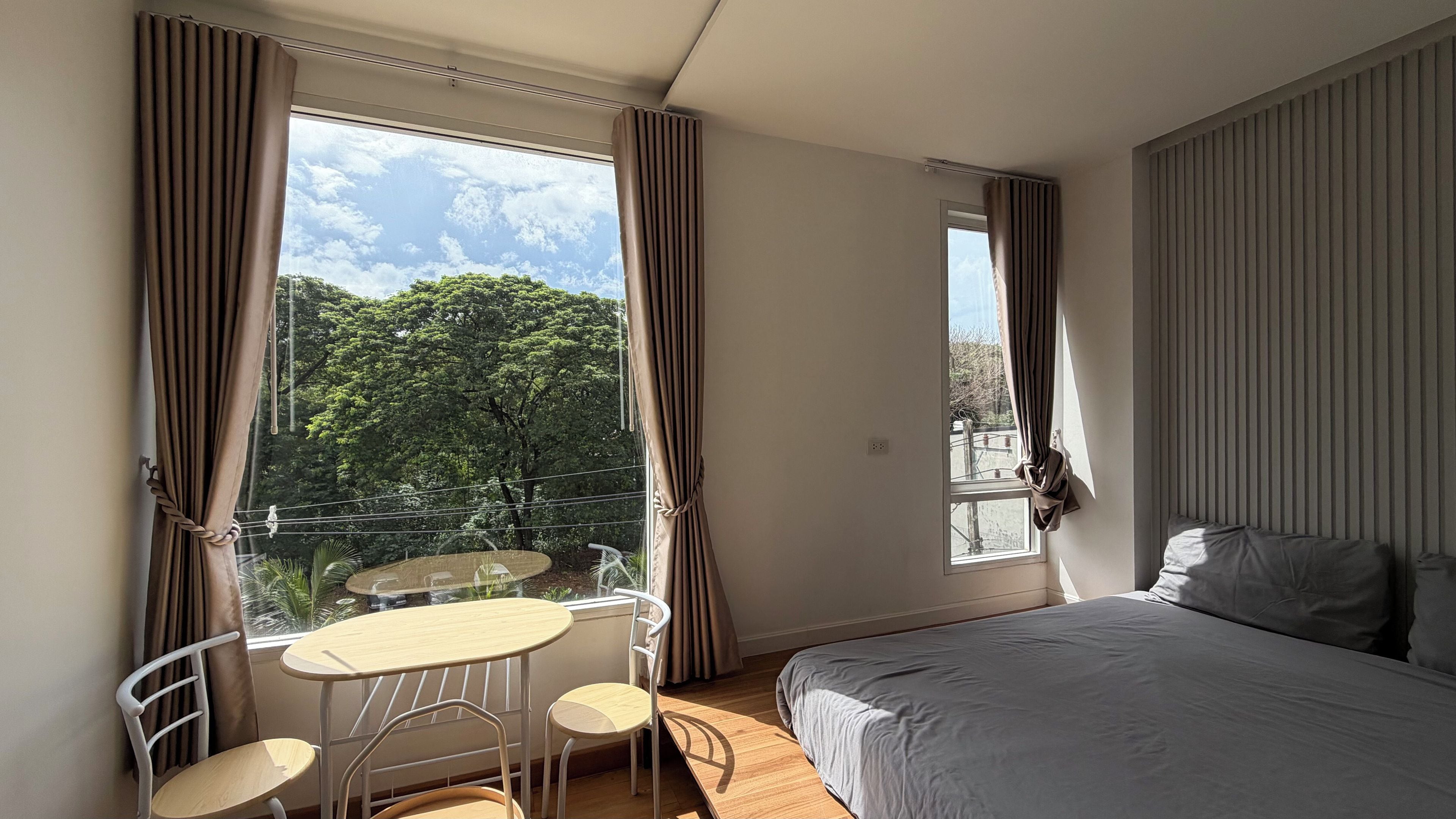 Un dormitorio con cama, una mesita con sillas y una ventana con cortinas.