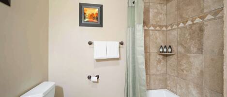 A bathroom with a toilet, a shower with a curtain, a framed picture on the wall, and a shelf with toiletries.