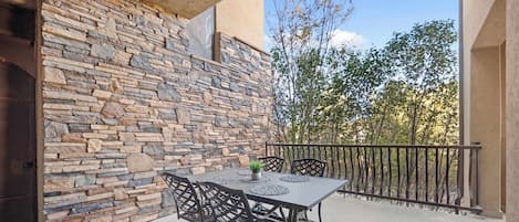An outdoor patio with a stone wall, a table with chairs, and a railing.